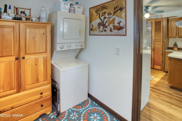 laundry room featuring laundry area, light wood-type flooring, a ceiling fan, stacked washer and clothes dryer, and baseboards