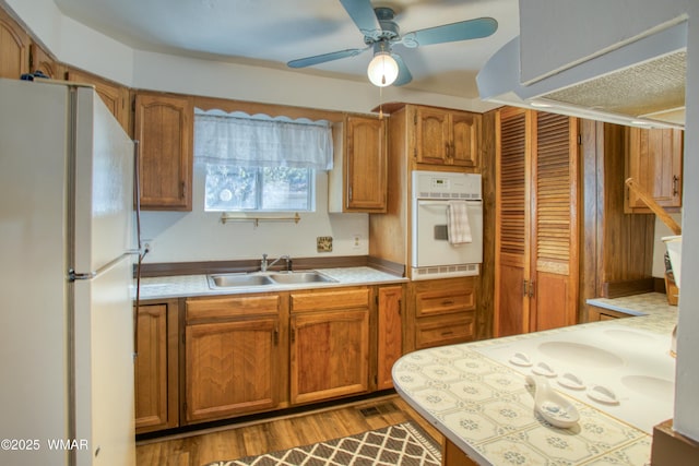 kitchen featuring light countertops, brown cabinets, a sink, and white appliances