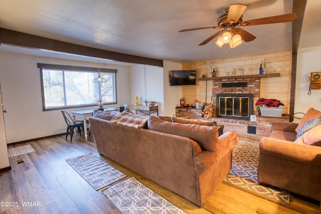 living area featuring a fireplace, a textured ceiling, wood finished floors, and ceiling fan