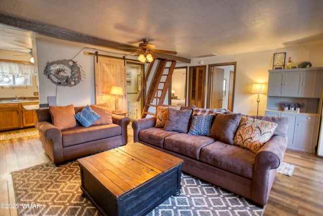 living area featuring stairway, a textured ceiling, a ceiling fan, a barn door, and wood finished floors