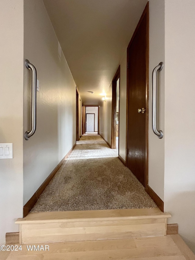 corridor with baseboards and light colored carpet