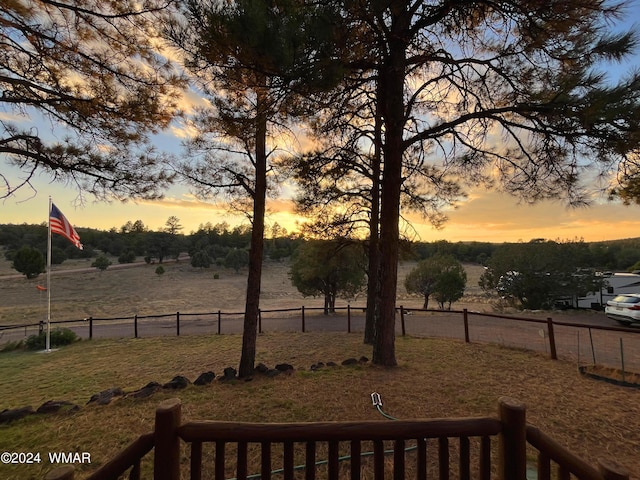 yard at dusk featuring a rural view and fence