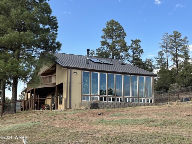 rear view of house featuring metal roof, a lawn, fence, and roof mounted solar panels