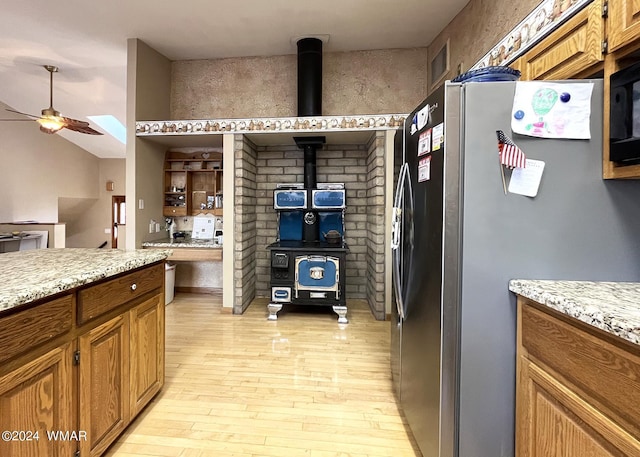 kitchen with ceiling fan, brown cabinets, a wood stove, and stainless steel fridge with ice dispenser