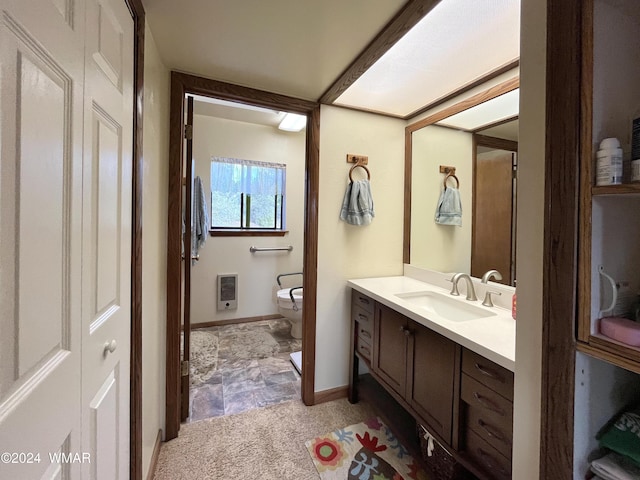 bathroom featuring heating unit, a closet, toilet, vanity, and baseboards