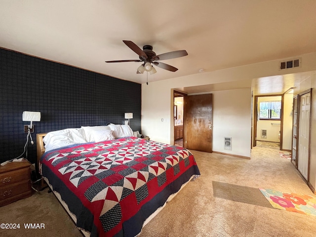 bedroom with connected bathroom, light carpet, an accent wall, visible vents, and baseboards