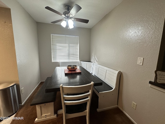 dining area featuring baseboards, dark carpet, a ceiling fan, and a textured wall