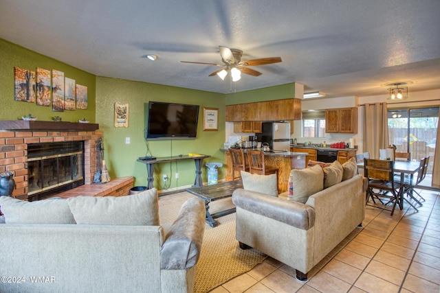 living room with a ceiling fan, a fireplace, a textured ceiling, and light tile patterned floors