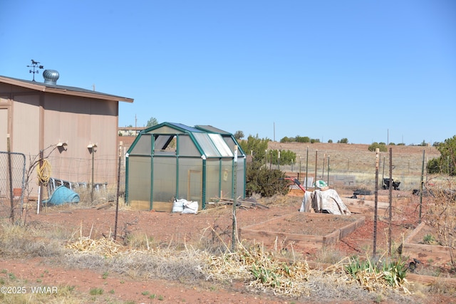 view of yard with fence, a greenhouse, a garden, and an outbuilding