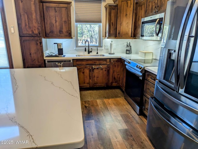 kitchen featuring stainless steel appliances, a sink, dark wood-style floors, and light stone countertops