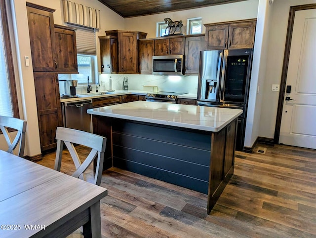 kitchen featuring dark brown cabinetry, dark wood-style floors, a kitchen island, appliances with stainless steel finishes, and a sink