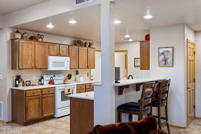 kitchen with brown cabinets, white appliances, a peninsula, and light countertops