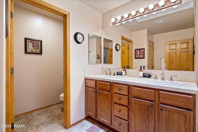 bathroom featuring baseboards, a sink, toilet, and double vanity