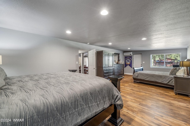 bedroom featuring a textured ceiling, a wall mounted air conditioner, wood finished floors, and recessed lighting