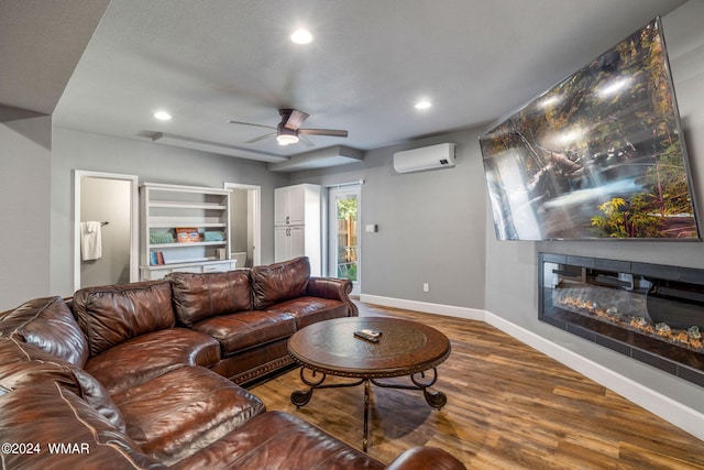 living room featuring recessed lighting, wood finished floors, baseboards, an AC wall unit, and a glass covered fireplace