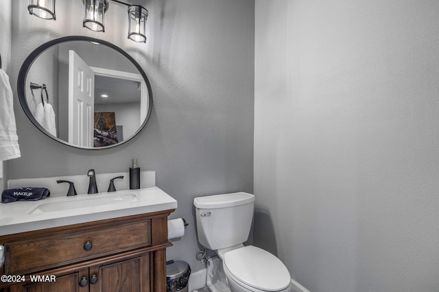 half bathroom with toilet, a textured wall, baseboards, and vanity