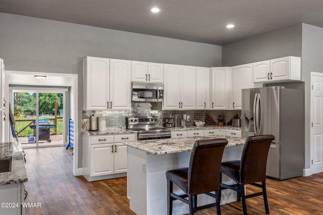 kitchen featuring light stone counters, a center island, a breakfast bar area, appliances with stainless steel finishes, and white cabinetry