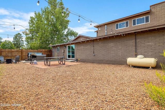 rear view of house with brick siding, a jacuzzi, fence, and a patio