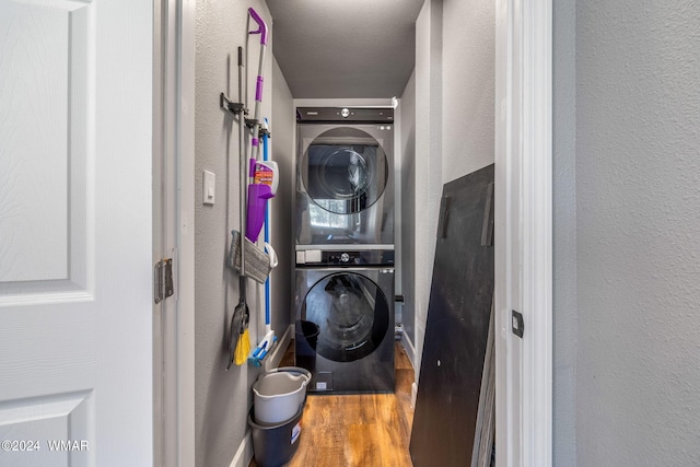 washroom with laundry area, a textured wall, stacked washer / dryer, and wood finished floors