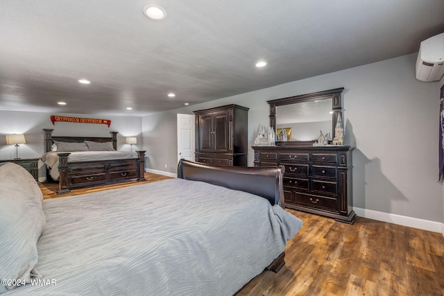 bedroom featuring a wall unit AC, baseboards, wood finished floors, and recessed lighting