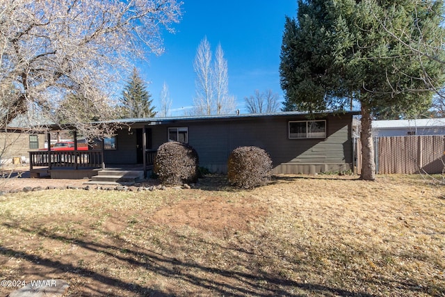 rear view of house featuring fence, a wooden deck, and a lawn