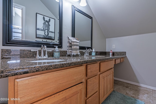 bathroom with vaulted ceiling, double vanity, a sink, and baseboards