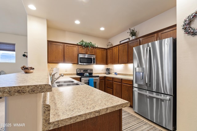 kitchen with stainless steel appliances, light countertops, brown cabinetry, a sink, and a peninsula