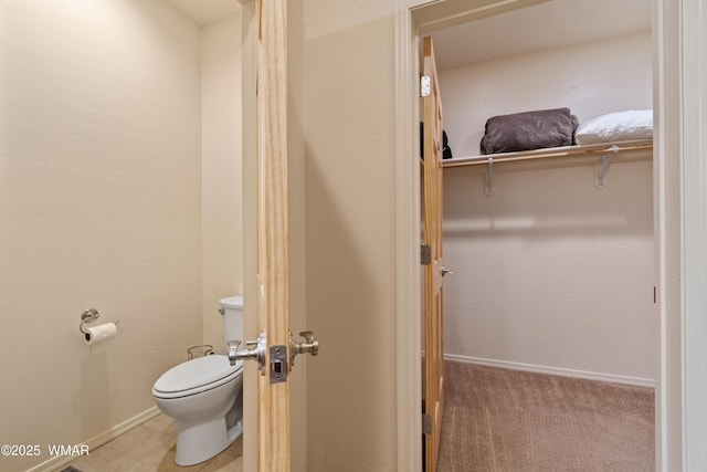 bathroom with toilet, baseboards, and a walk in closet