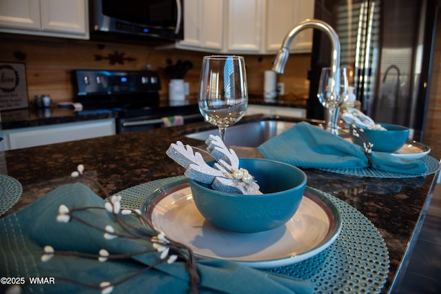 interior details featuring black appliances, dark stone countertops, a sink, and white cabinetry