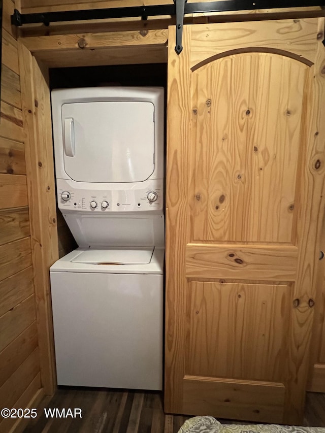 clothes washing area featuring laundry area, wood walls, stacked washer / dryer, and wood finished floors