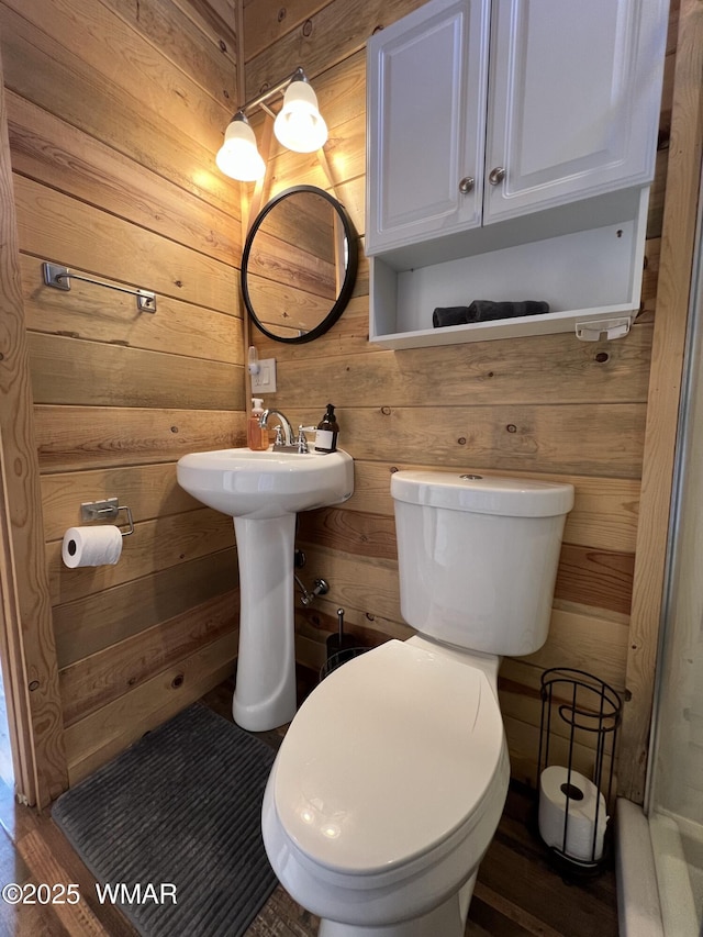 bathroom with wood walls, a sink, and toilet