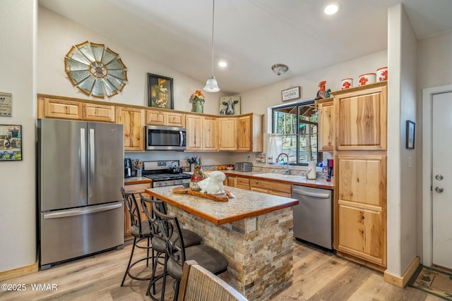kitchen featuring stainless steel appliances, a sink, hanging light fixtures, light countertops, and light wood-type flooring