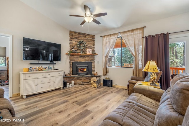 living area featuring light wood finished floors, baseboards, lofted ceiling, ceiling fan, and a stone fireplace