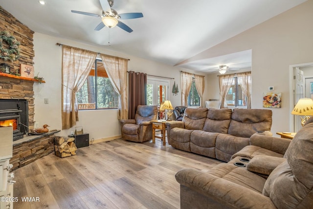 living room featuring lofted ceiling, ceiling fan, a stone fireplace, and light wood-type flooring