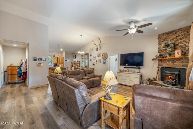 living room with baseboards, lofted ceiling, a stone fireplace, light wood-style floors, and ceiling fan with notable chandelier