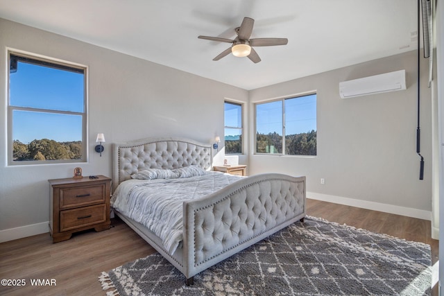 bedroom featuring a wall unit AC, wood finished floors, and baseboards