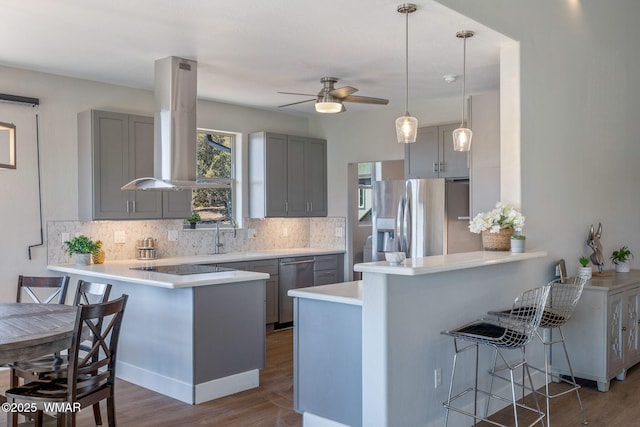 kitchen with light countertops, gray cabinetry, appliances with stainless steel finishes, island range hood, and a peninsula