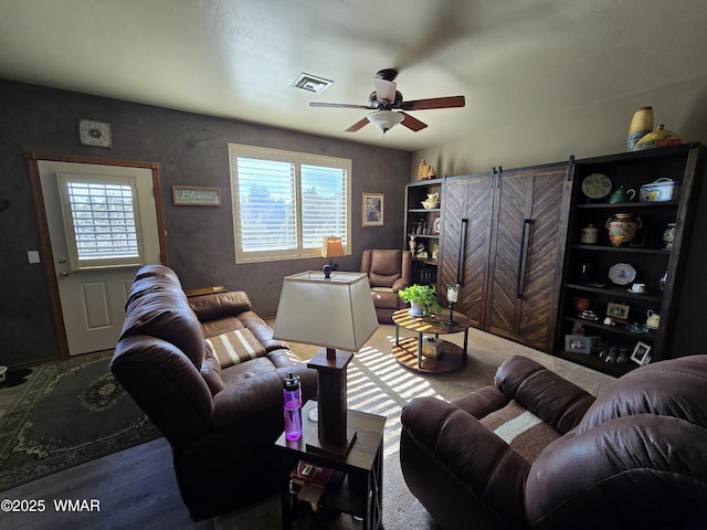 living room with a ceiling fan, a healthy amount of sunlight, visible vents, and a barn door