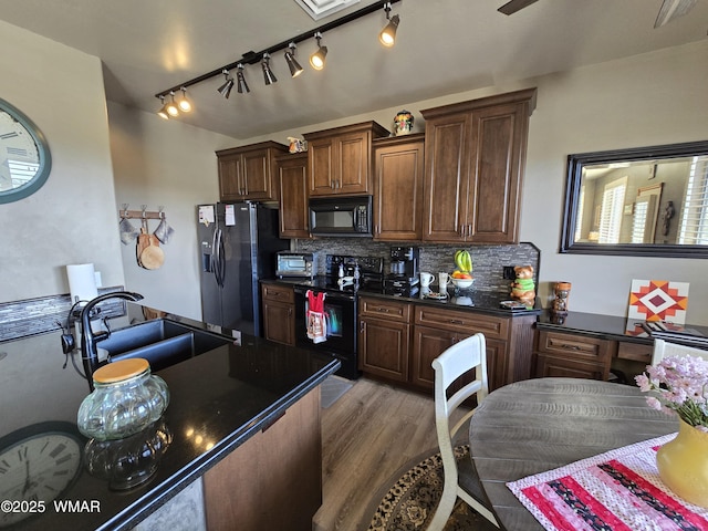 kitchen with a sink, light wood-style floors, backsplash, black appliances, and dark countertops