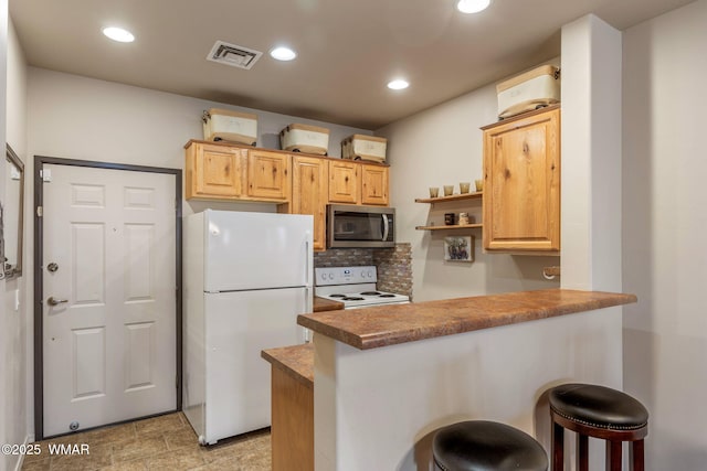 kitchen featuring white appliances, a peninsula, light brown cabinetry, visible vents, and a breakfast bar