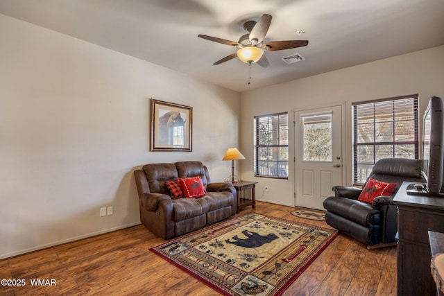 living room featuring wood finished floors, ceiling fan, baseboards, and visible vents