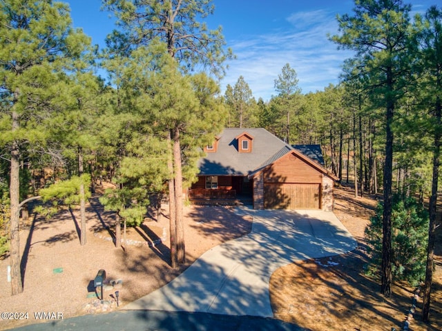 chalet / cabin featuring a garage, stone siding, driveway, and a forest view