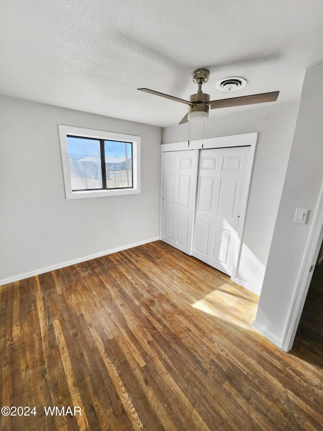 unfurnished bedroom with wood finished floors, a ceiling fan, visible vents, baseboards, and a closet