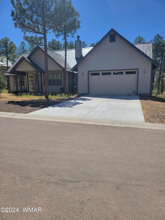 view of front of home with concrete driveway, metal roof, a chimney, and an attached garage