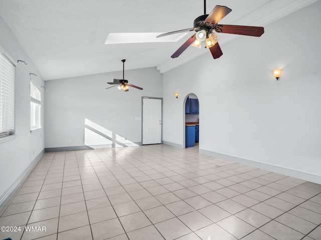 spare room with a skylight, arched walkways, baseboards, and light tile patterned floors