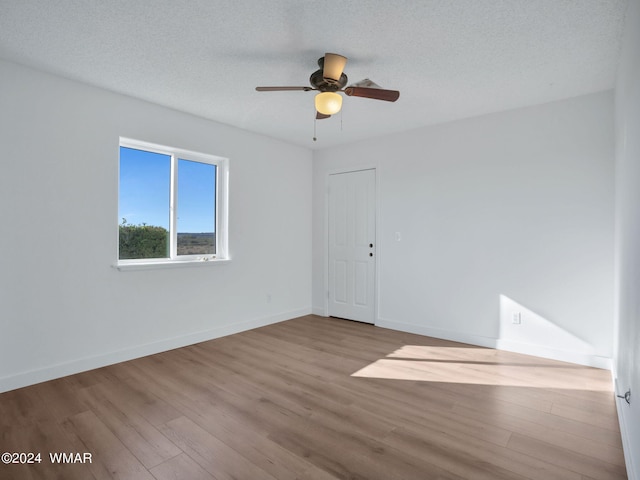 empty room with light wood-style floors, a ceiling fan, baseboards, and a textured ceiling