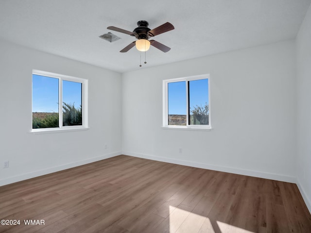 spare room featuring a ceiling fan, visible vents, baseboards, and wood finished floors