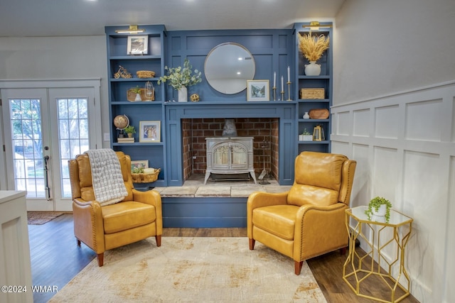 sitting room featuring built in shelves, wood finished floors, a wood stove, and a decorative wall