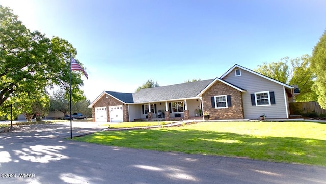 ranch-style home with driveway, stone siding, an attached garage, covered porch, and a front yard