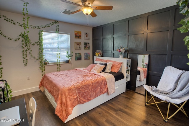 bedroom with dark wood-style floors, visible vents, a decorative wall, a ceiling fan, and a textured ceiling